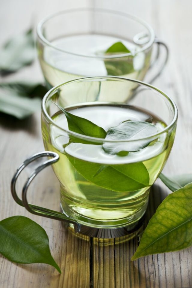 Šálky so zeleným čajom a lístkami čajovníka
