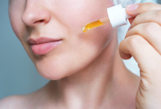 Female face and dropper with moisturizing serum close up on a gray background.